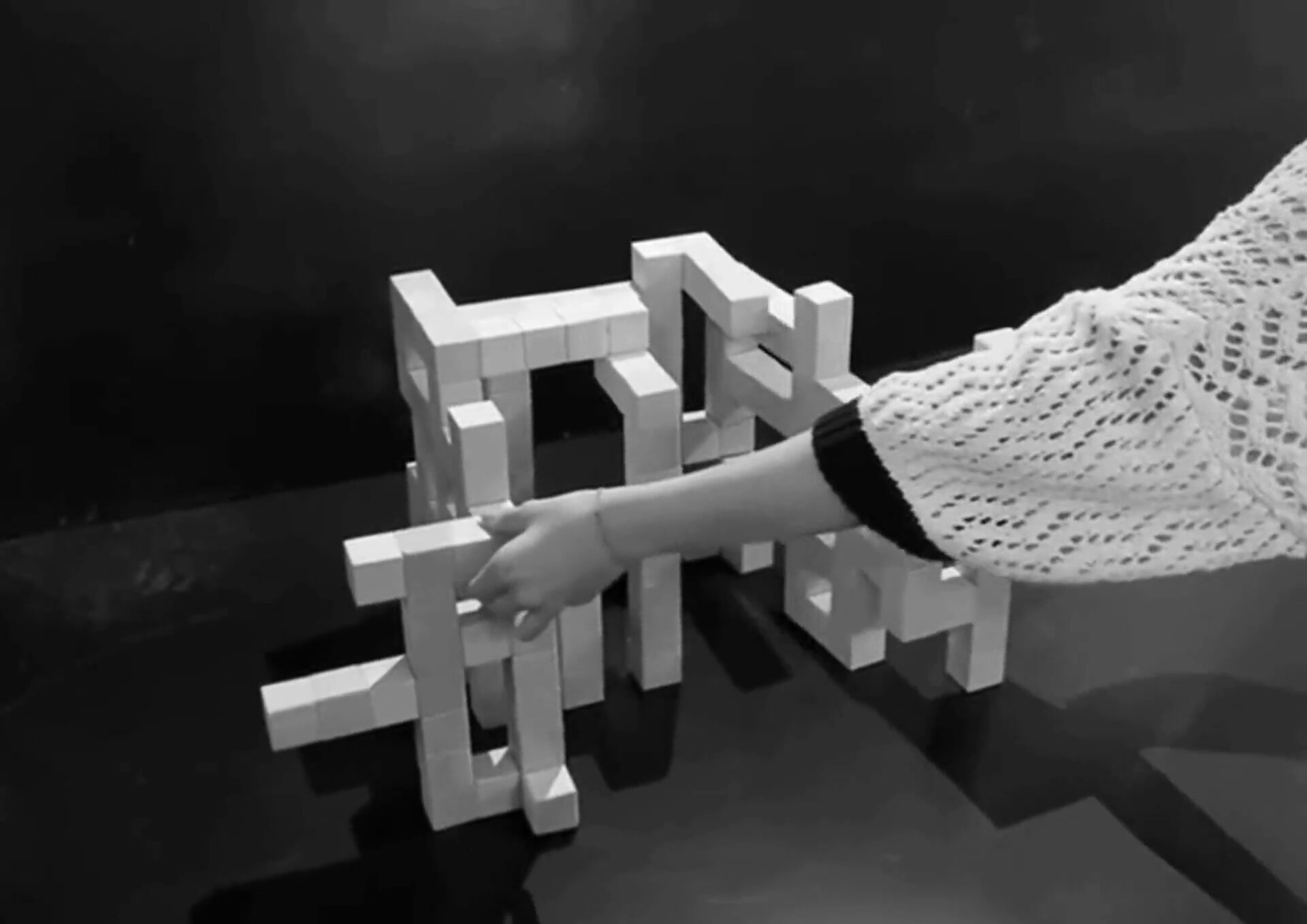 Una mano ensamblando los volúmenes de madera entrelazados de la maqueta Hellytown